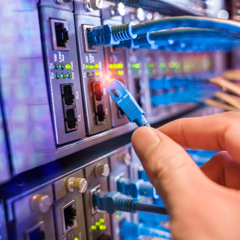 man working in network server room with fiber optic hub for digital communications and internet